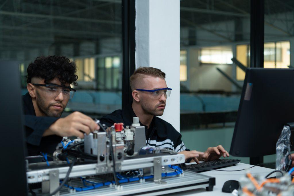 The robotic hand technology teacher is instructing new students on how to use electronic circuit boards and robotic hand commands for a variety of industrial applications.